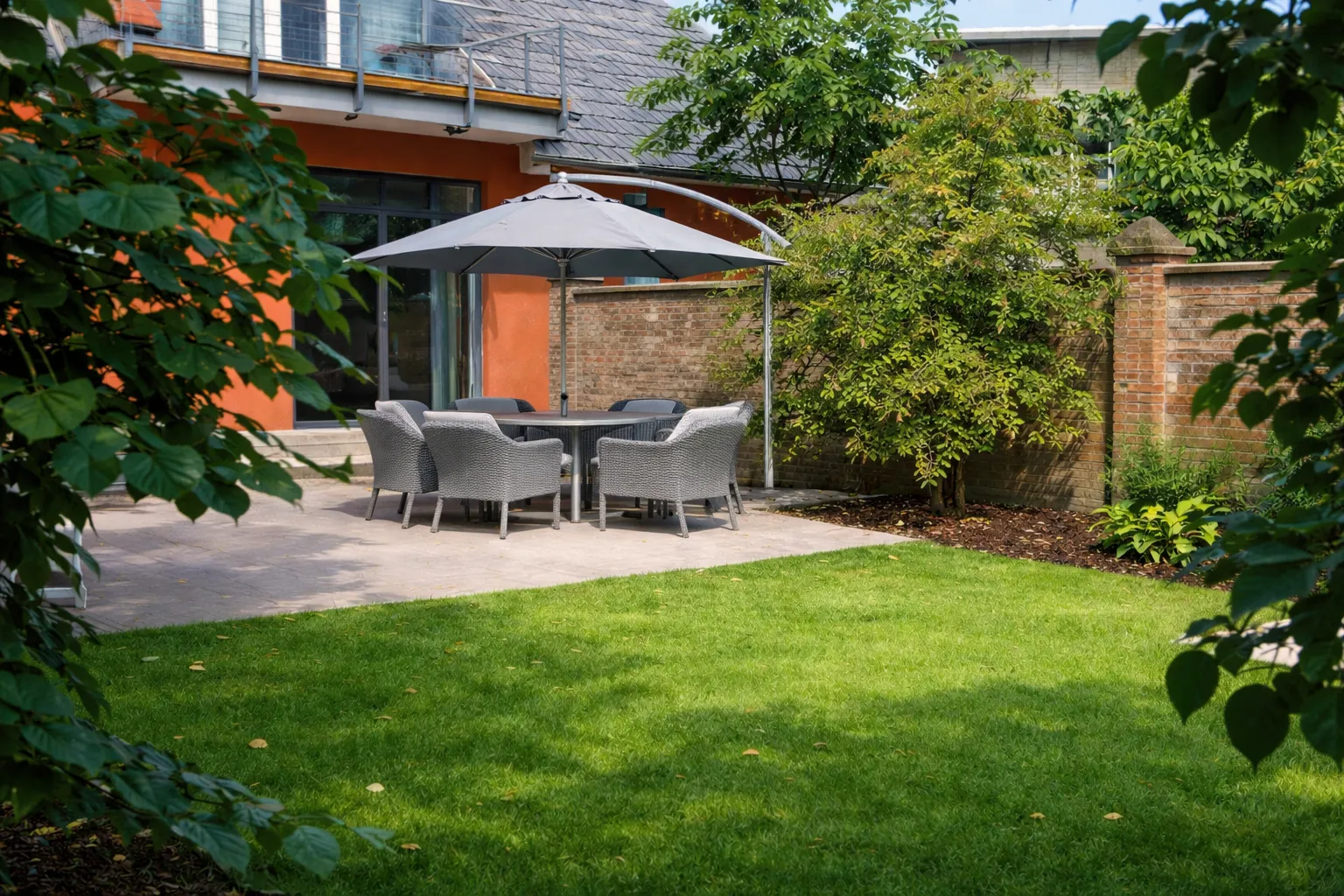 Große Terrasse mit Gartenmöbeln, Sonnenschirm und grünem Rasen hinter dem Ferienhaus Roter Seestern